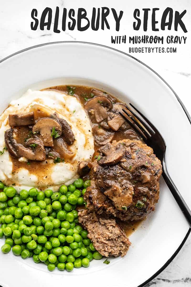 A plate full of Salisbury Steak, Mushroom Gravy, Mashed Potatoes, and Green Peas