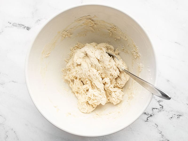 Shaggy pizza dough in the bowl with a spoon.