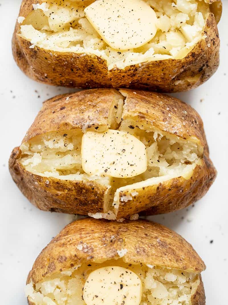 Overhead view of baked potatoes lined up, opened and fluffed, with pats of butter inside