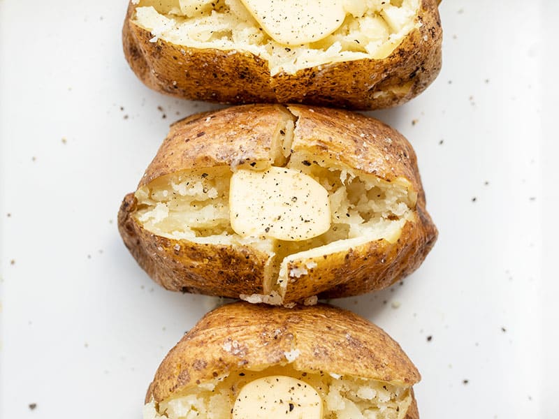 Baked potatoes lined up, seasoned with pepper and butter