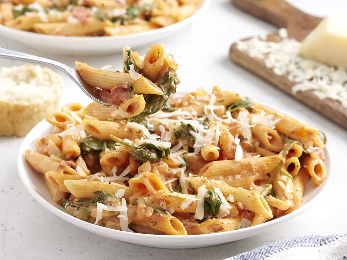 Side view of tomato spinach pasta on a plate with a fork taking some.