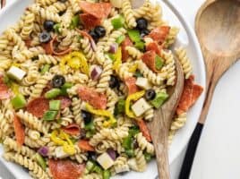 Close up of a serving bowl of pizza pasta salad, a wooden spoon in the side