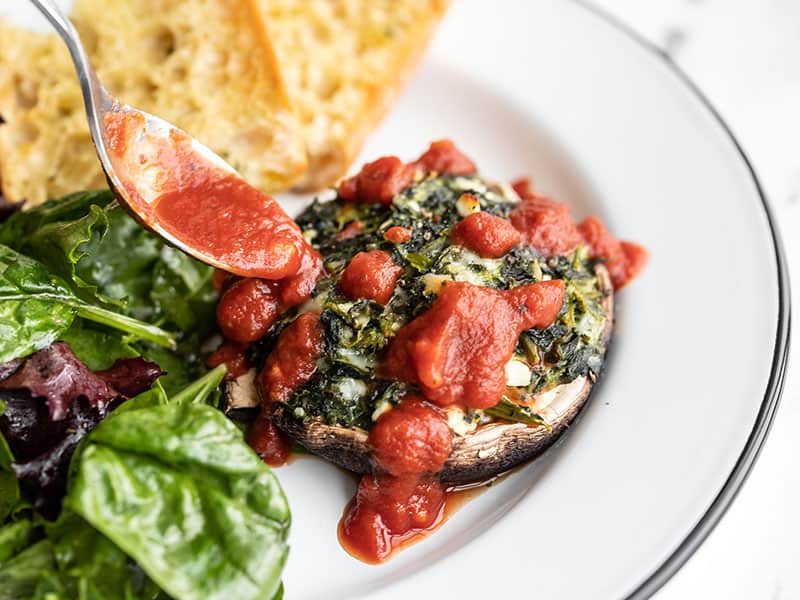 Marinara being spooned over a spinach stuffed portobello mushroom