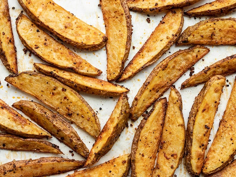 Baked steak fries close up on a parchment lined baking sheet