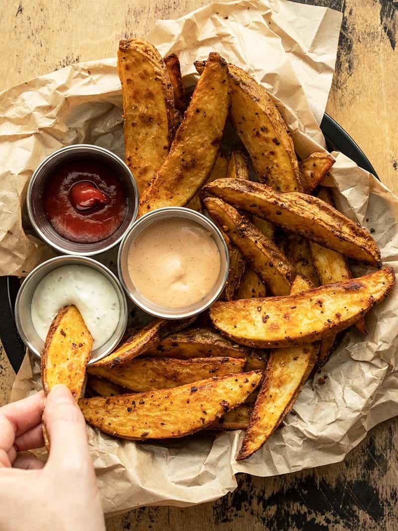 Steak fries on a paper lined plate, one being dipped into one of three dipping sauces