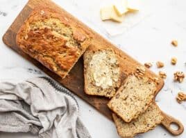 A loaf of yogurt banana bread on a wooden cutting board, a few slices scattered, one smeared with butter