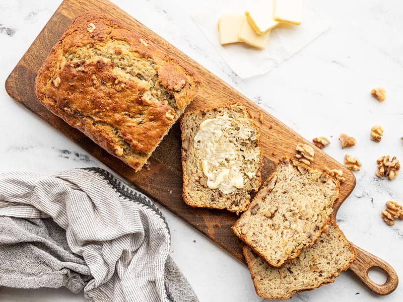 A loaf of yogurt banana bread on a wooden cutting board, a few slices scattered, one smeared with butter