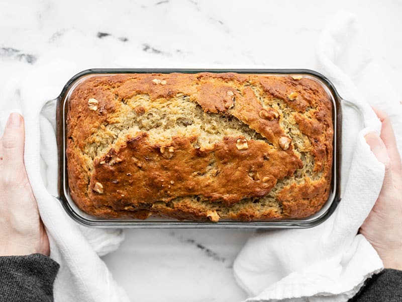 Baked yogurt banana bread being held by two hands with white towels