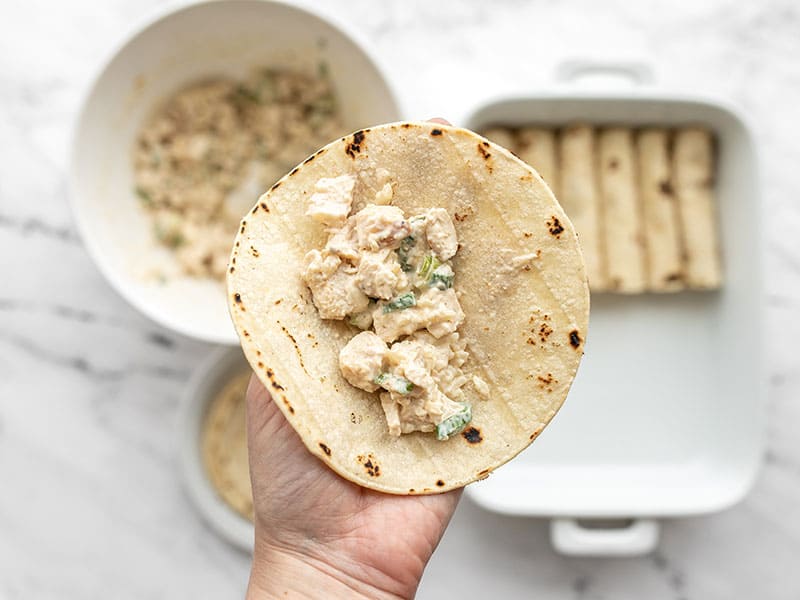 chicken filling in one tortilla, the bowl and casserole dish in the background