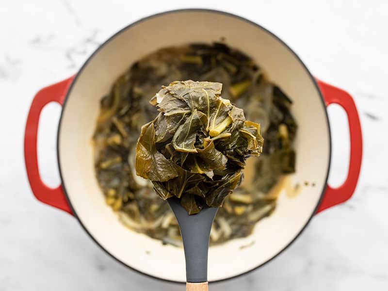 A ladle full of Jerk Seasoned Collard Greens hovering over the pot