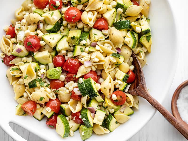 Close up of a bowl of Summer Sweet Corn Salad with a wooden spoon in the middle