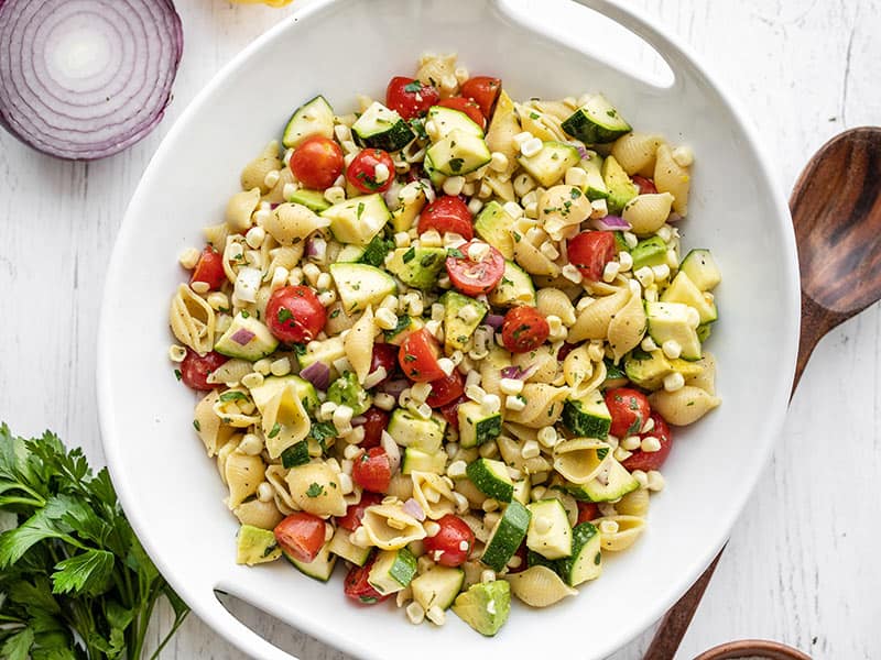 Overhead view of a serving bowl of summer sweet corn salad with a wooden spoon on the side