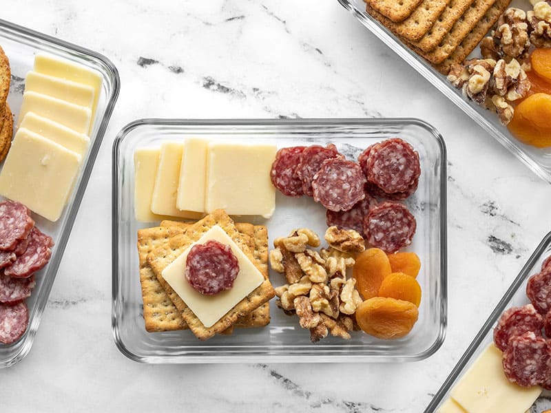 Overhead view of one Cheese board Lunch Box with a cracker stacked with cheese and salami.