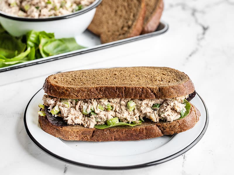 A classic tuna salad sandwich front view with sandwich fixings in the background