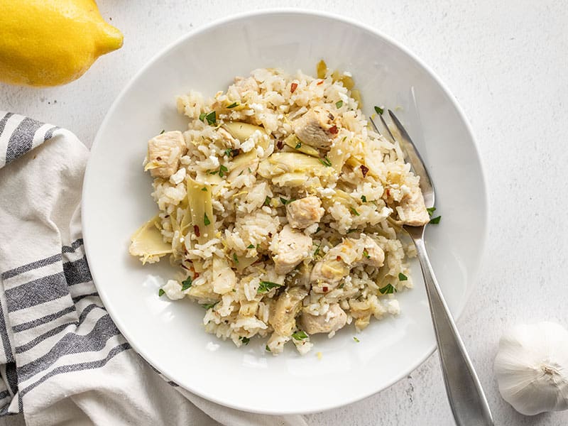 A bowl of one pot lemon artichoke chicken and rice with a fork in the side