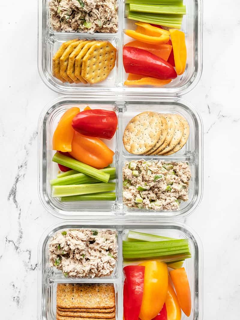 Three divided glass meal prep containers with tuna salad, crackers, and vegetables