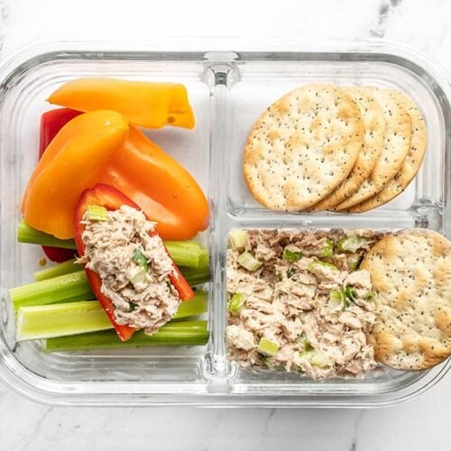 A tuna salad lunch box with tuna in a pepper and a cracker tipping into the salad