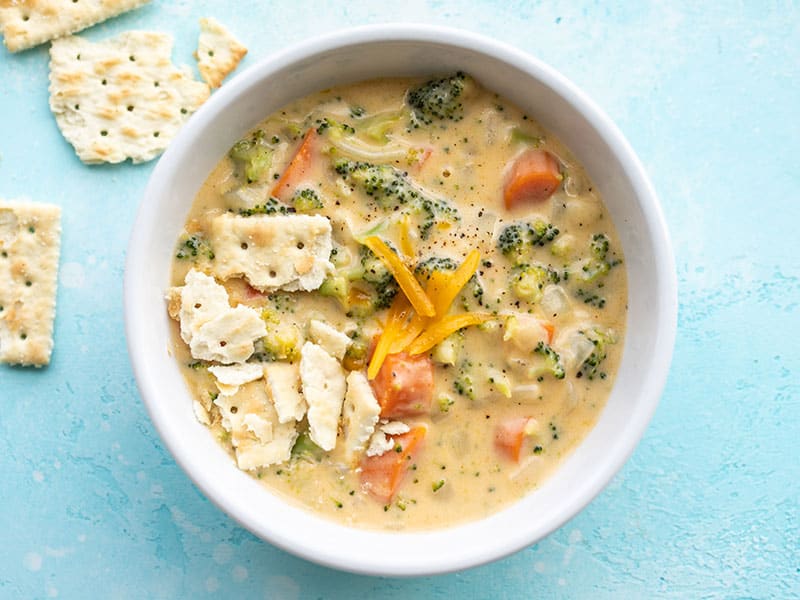 Overhead view of a bowl of broccoli cheddar soup with saltine crackers