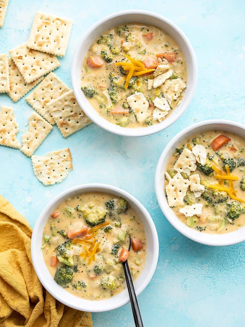 Three bowls of Broccoli Cheddar Soup with saltine crackers on the side