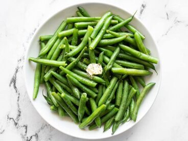 Overhead of a bowl of steamed green beans with butter, salt, and pepper.