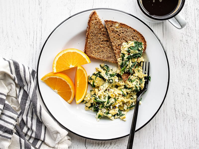 Scrambled eggs with spinach and feta on a plate with toast, half piled onto a slice of toast