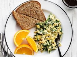 A plate full of scrambled eggs with spinach and feta, toast, and orange slices