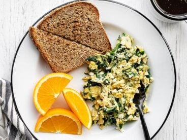 A plate full of scrambled eggs with spinach and feta, toast, and orange slices