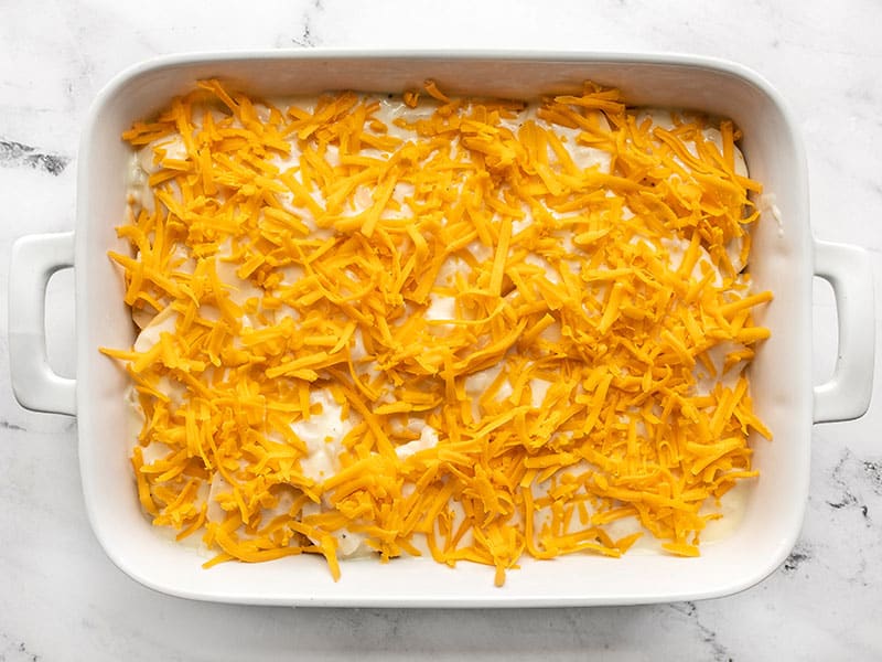 shredded cheese on potatoes in casserole dish