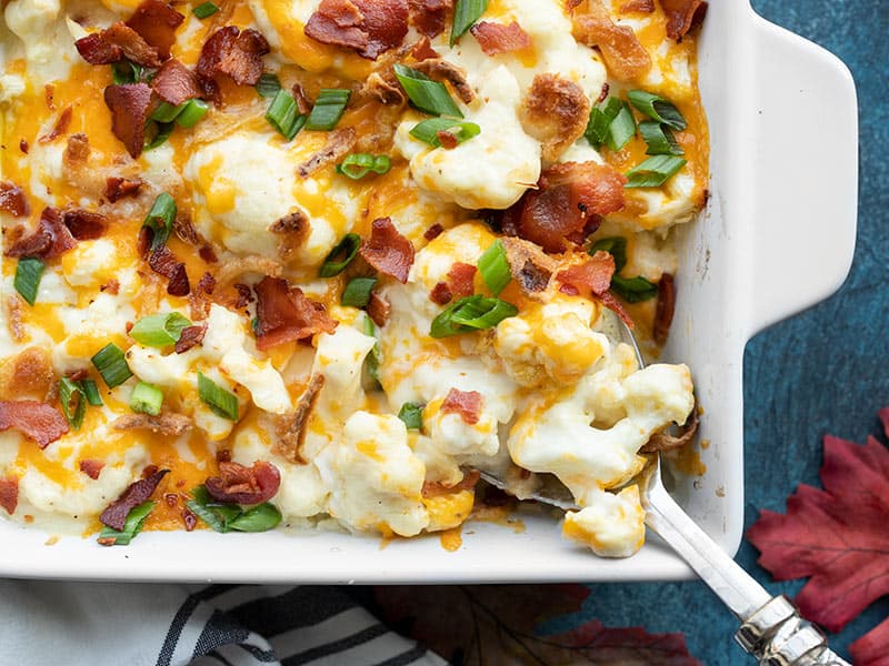 close up of cheesy loaded cauliflower casserole being scooped out of the dish