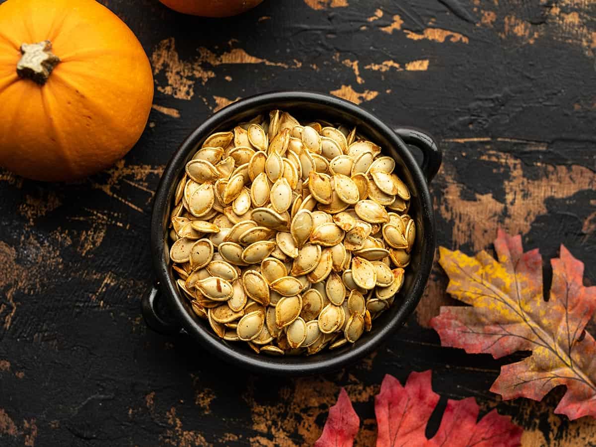 Overhead view of a bowl full of roasted pumpkin seeds on a wooden background. 