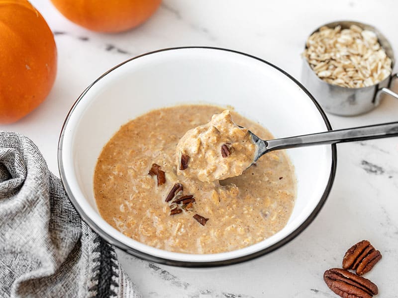 Side view of a spoon lifting some pumpkin pie overnight oats out of the bowl