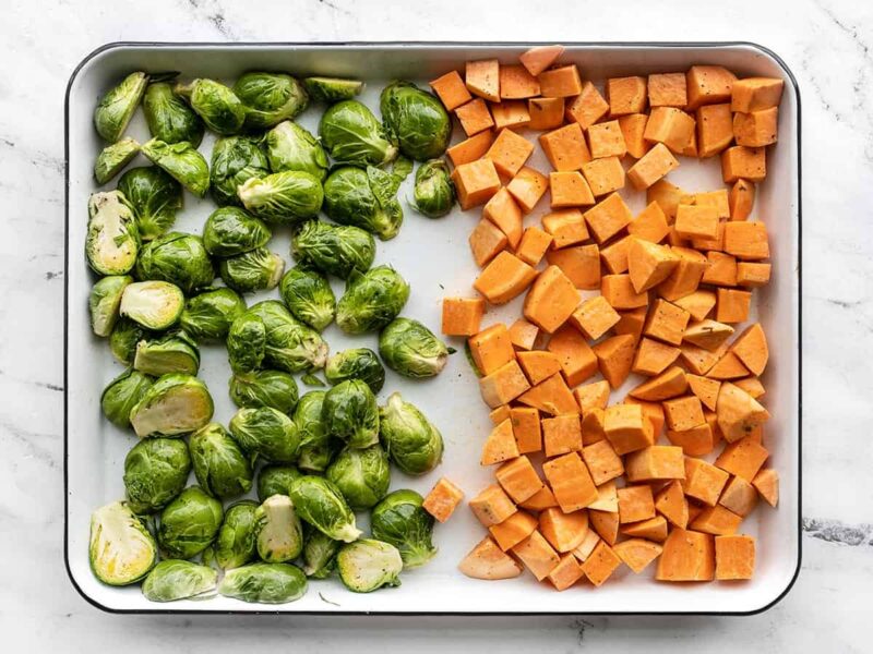 Prepped Brussels sprouts and sweet potatoes on a baking sheet