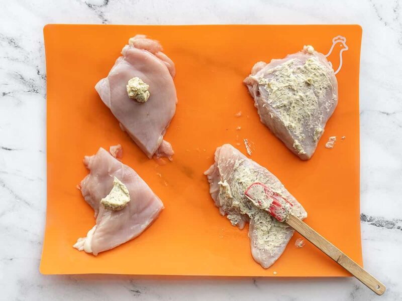 Herb butter being spread over the chicken breasts