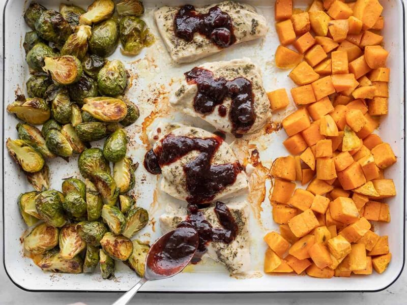 Cranberry balsamic sauce being spooned over the chicken on the baking sheet