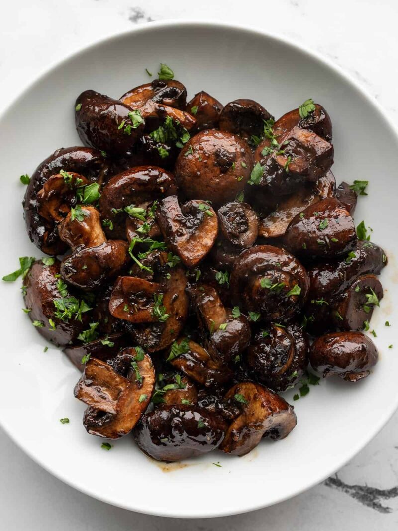 Overhead view of balsamic roasted mushrooms in a white bowl, garnished with parsley