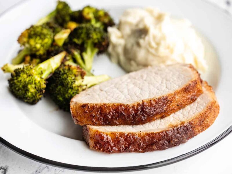 Two slices of pork loin on a plate with broccoli and mashed potatoes, viewed from the side