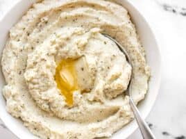 Garlic Herb Mashed Cauliflower in a bowl with a spoon and melted butter