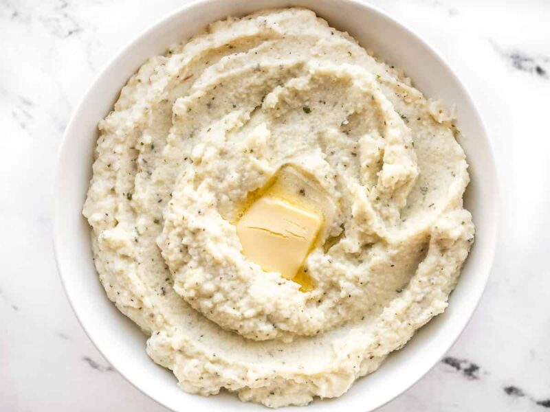 A bowl full of garlic herb mashed cauliflower with a pat of butter in the center