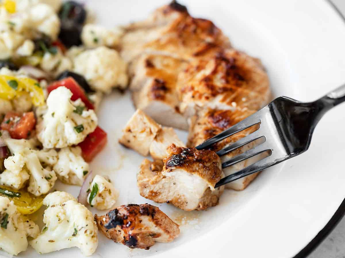 A fork picking up a slice of garlic marinated chicken from a plate