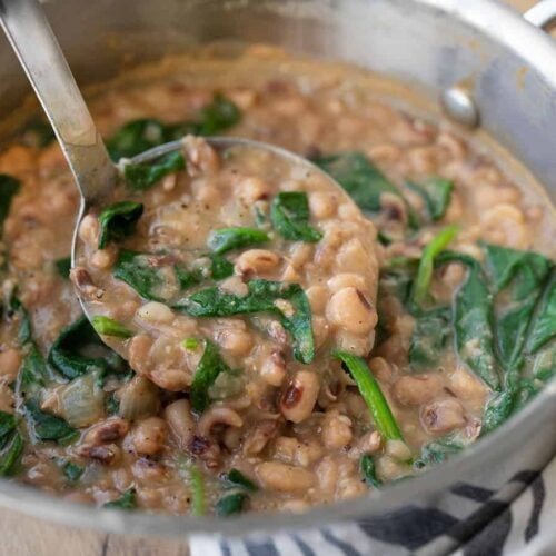 Side view of a ladle lifting some black eyed peas and greens from the pot