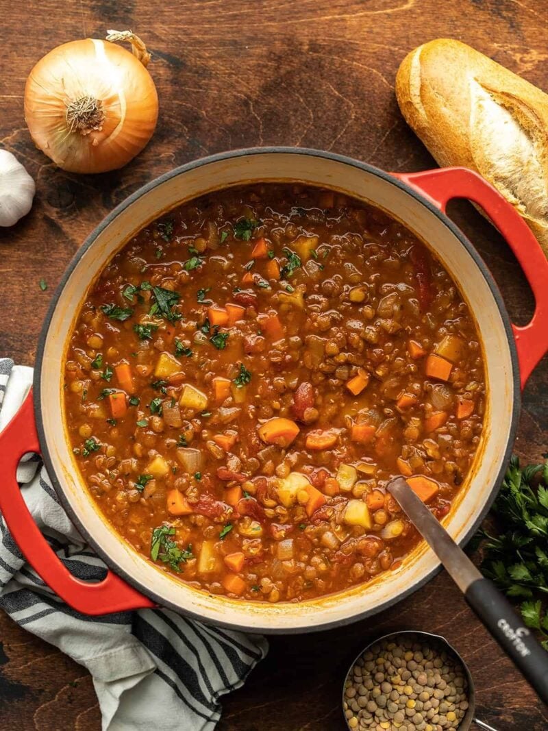 Tomato lentil soup in the pot with bread and vegetables on the sides