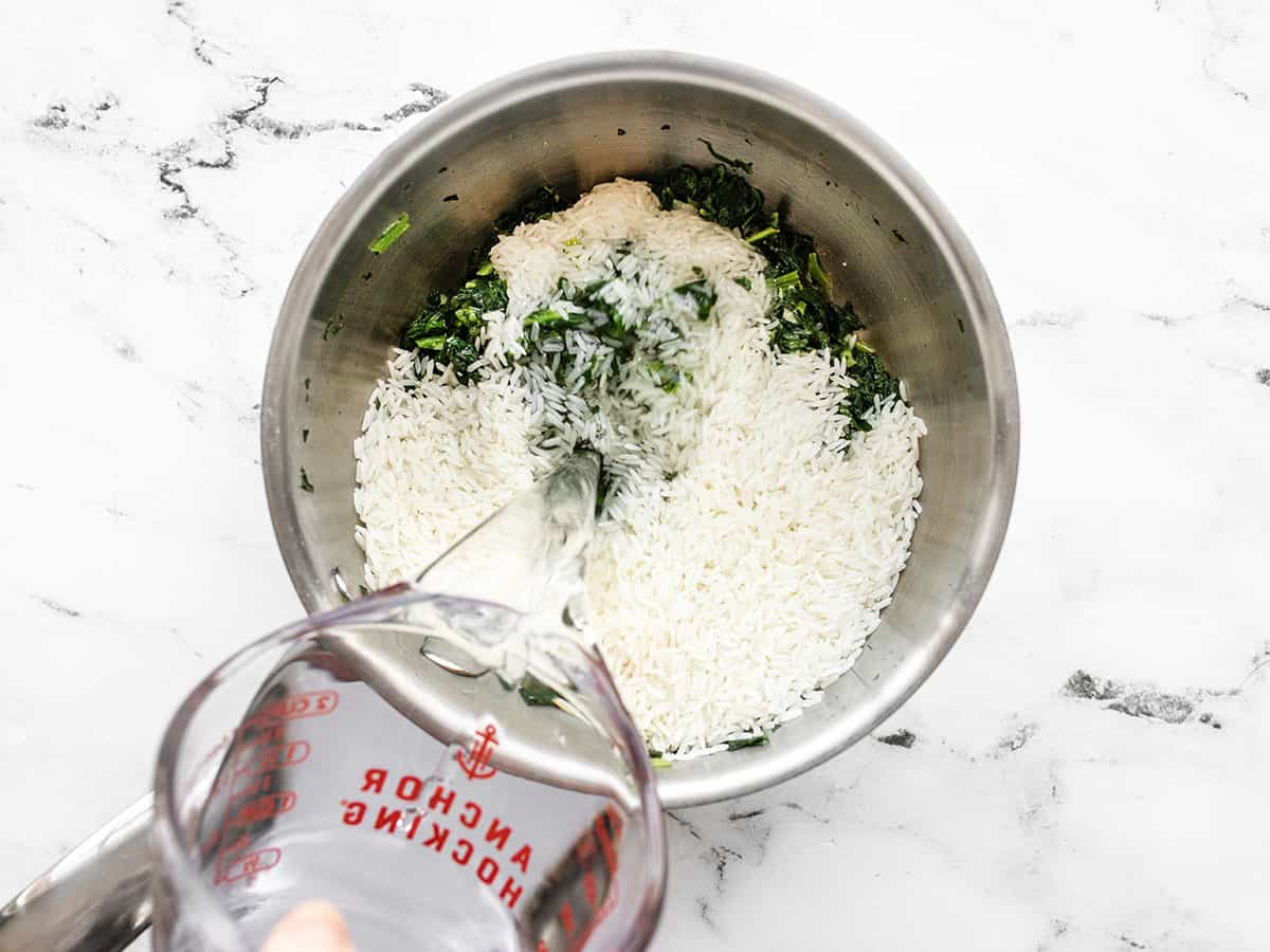 water being poured into the sauce pot with the rice and spinach