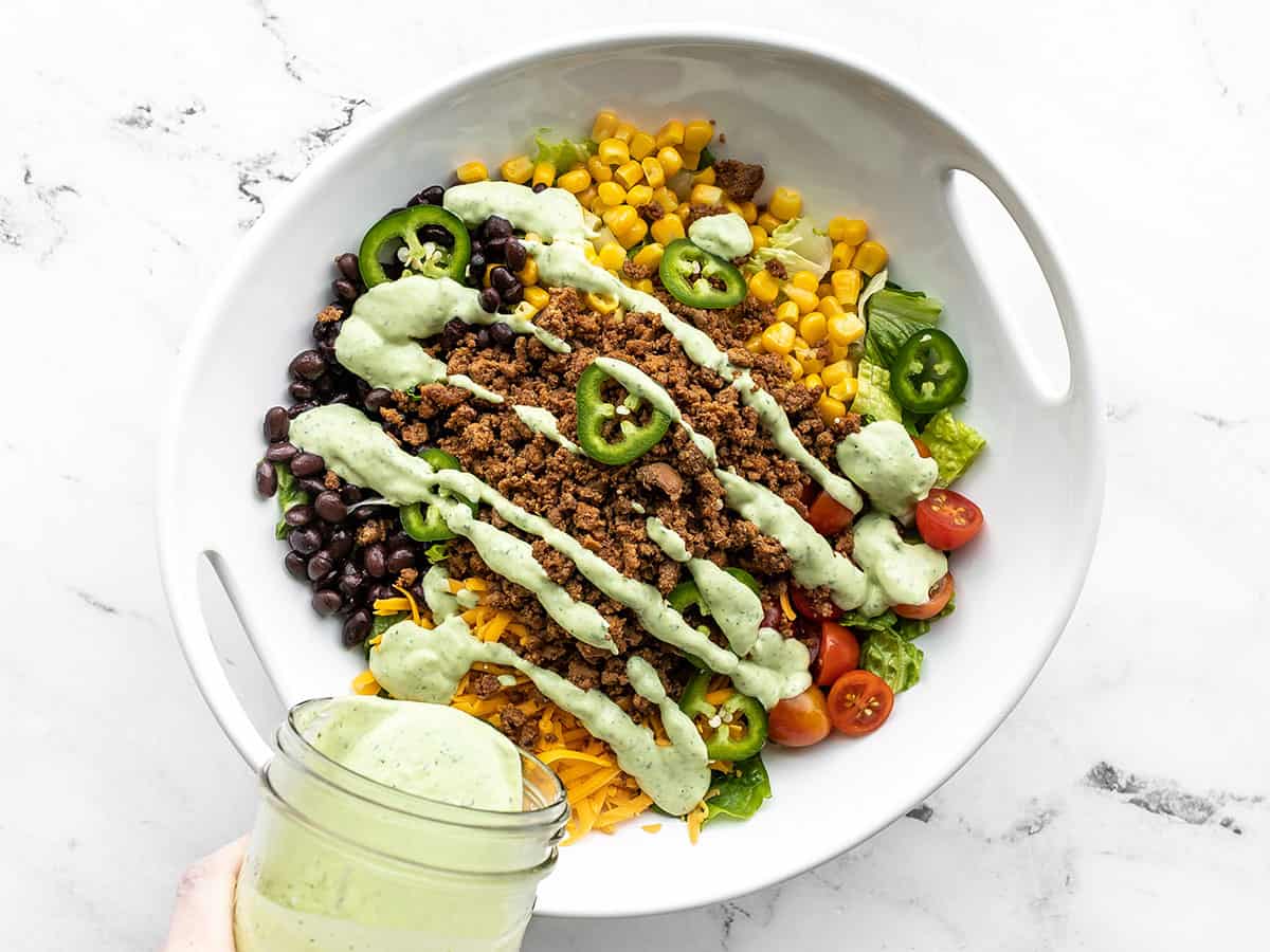 Creamy avocado dressing being poured over the salad