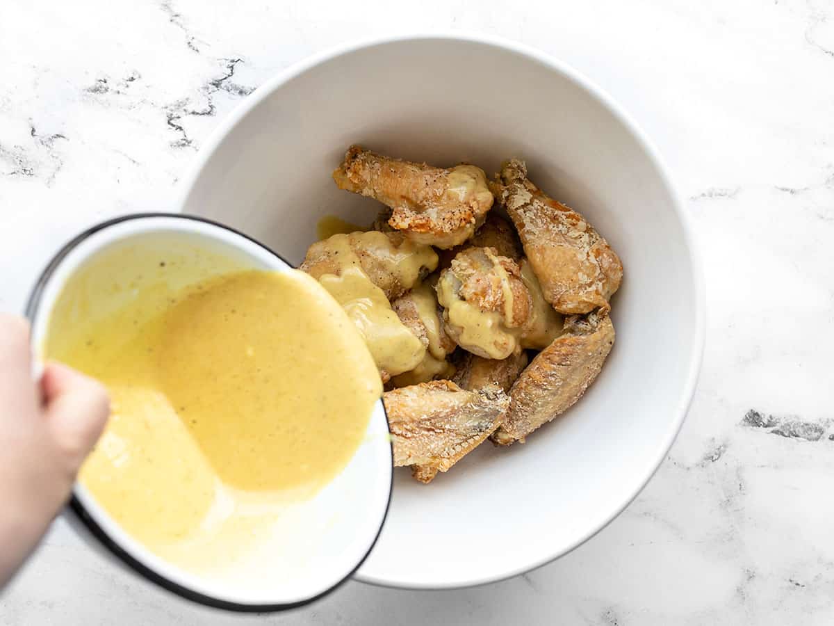 honey mustard being poured over baked wings in a bowl