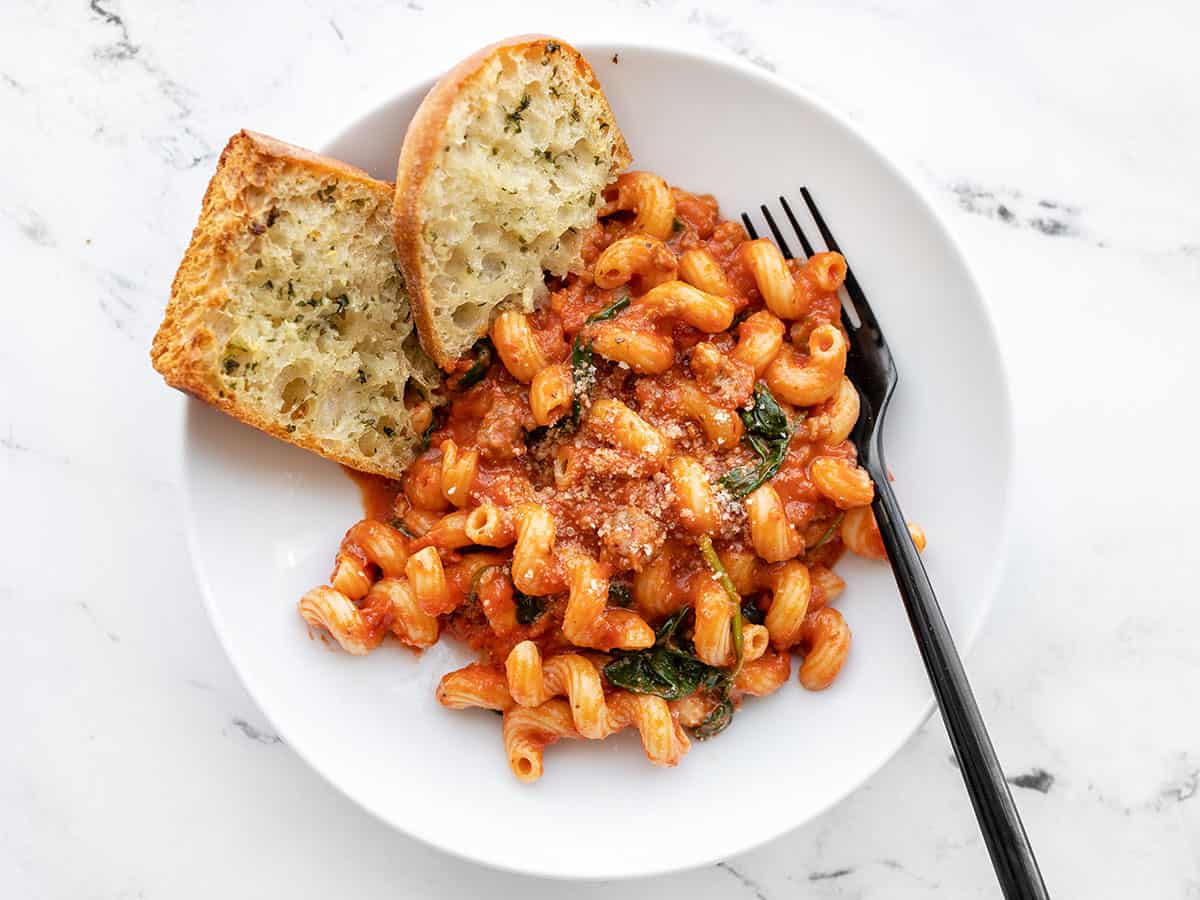 A bowl full of Creamy Tomato Pasta with Sausage with garlic bread and a fork