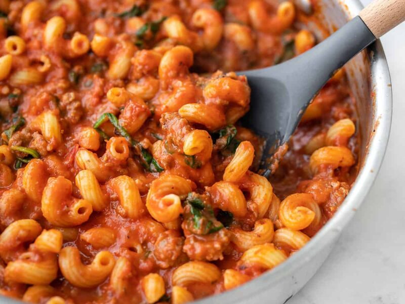 Close up side view of a skillet full of creamy tomato pasta with sausage