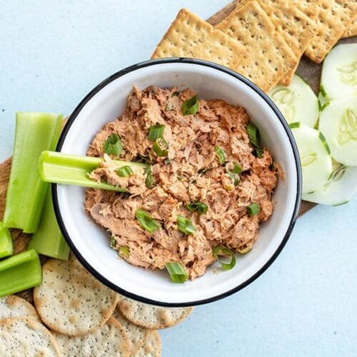 A bowl of gochujang tuna salad surrounded by vegetables and a celery stick dipped in the center