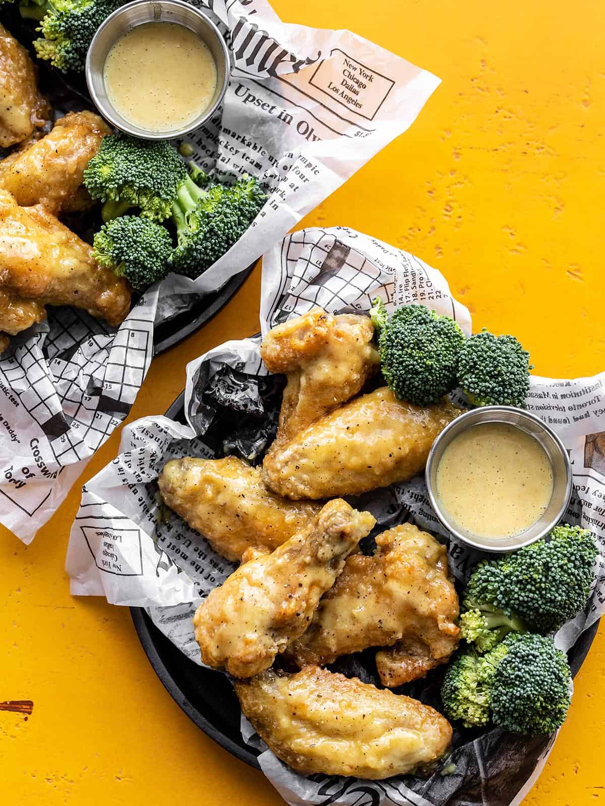 Two trays with honey mustard wings, broccoli, and cups of sauce