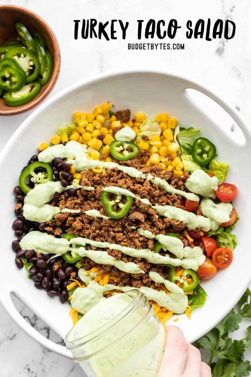 avocado dressing being poured over a turkey taco salad