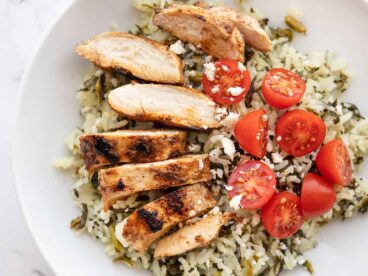 Sliced Yogurt Marinated chicken on a bed of spinach rice with tomatoes and feta